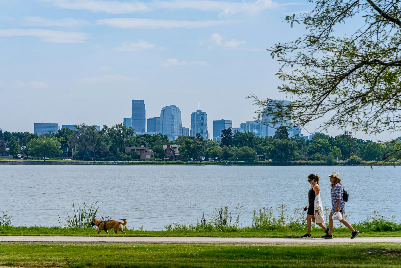 Walkers and a dog on the Sloan’s Lake path, with the downtown Denver skyline across the water